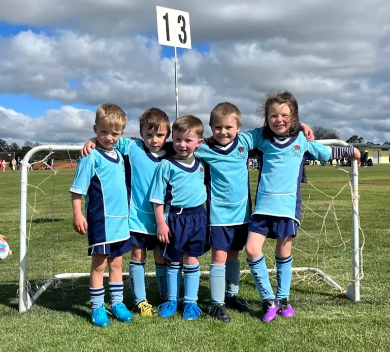 Five junior soccer players in light blue, in front of small goal